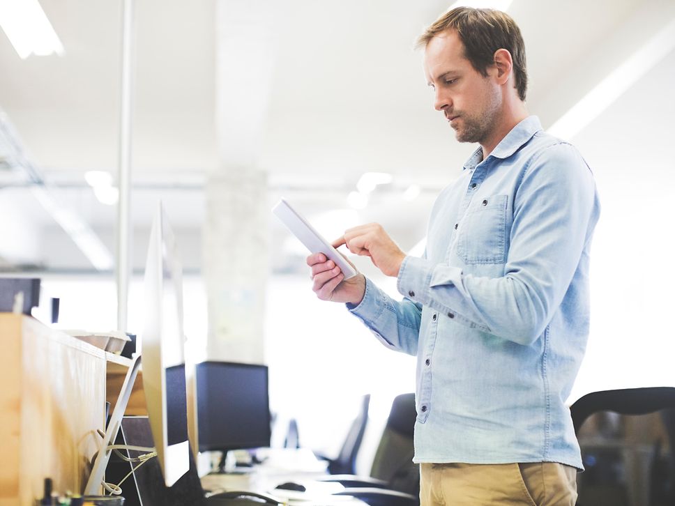 Ein Mann steht mitten im Büro und blickt konzentriert auf sein Tablet
