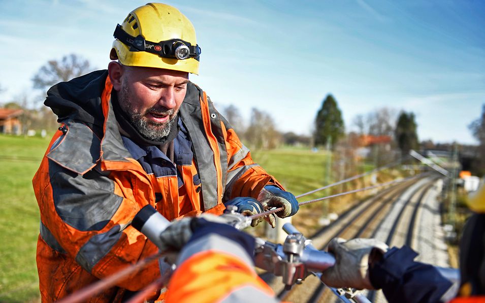 Ein DB-Mitarbeiter in oranger Arbeitskleidung arbeitet an den Gleisen